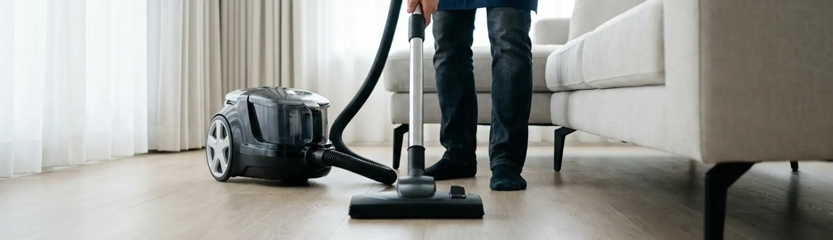Professional house cleaner vacuuming a living room floor with a canister vacuum cleaner, Worcester, MA.