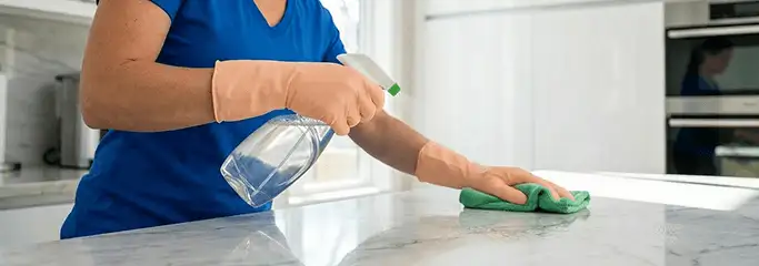 Maid service worker spraying and wiping a kitchen countertop with a microfiber cloth for sanitizing, Worcester, MA.