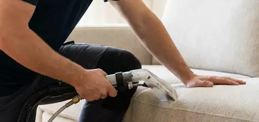 Professional upholstery cleaner deep-cleaning a fabric sofa with a handheld extraction tool, Worcester, MA.