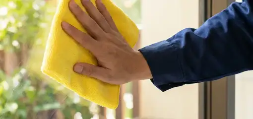 House cleaner wiping a glass window with a yellow microfiber cloth for streak-free cleaning, Worcester, MA.